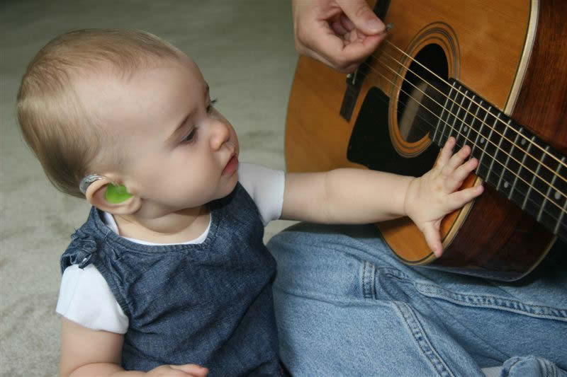 Toddler with hearing aid touching guitar